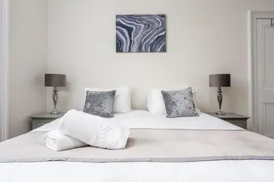 a white bedroom with a white bed with two lamps at Cuthbert House in Prestwick