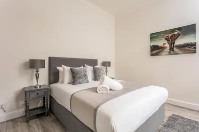 a bedroom with a white bed with a painting on the wall at Cuthbert House in Prestwick