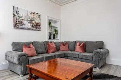a living room with a gray couch with red pillows at Cuthbert House in Prestwick