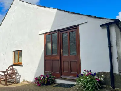 a small white house with a wooden door and a chair at Fell View Bassenthwaite, rural location on a working farm in the fells in Bassenthwaite
