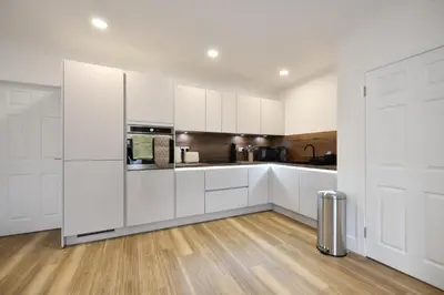 a white kitchen with white cabinets and a hardwood floor at Troon Portland Apt A in Troon