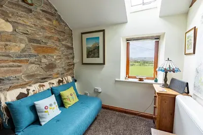 a living room with a blue couch and a stone wall at HIGH TREES BYRE - Two bed Cottage with Log Burner & Incredible Views in Workington