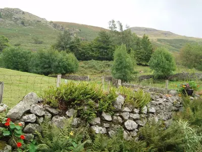a stone retaining wall in a garden with flowers at Fisher-gill Camping Barn in Thirlmere