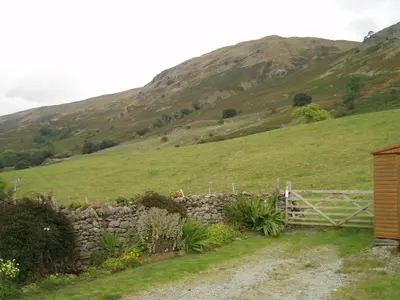 a stone fence in front of a grassy hill at Fisher-gill Camping Barn in Thirlmere