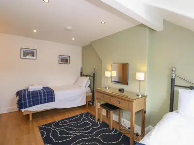 a bedroom with two beds and a desk with a mirror at Baystones in Keswick