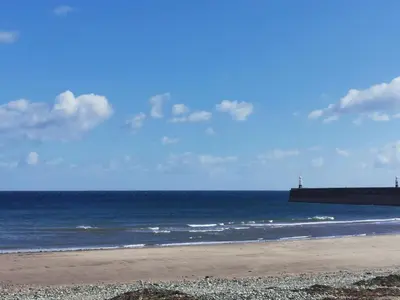 a beach with the ocean and a pier in the background at Antrim Holiday Apartment in Ramsey