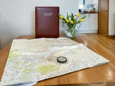 a map on a table with a clock and a vase of flowers at Pippa's Cottage - Uk42332 in Little Blencow