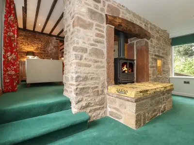a living room with a stone fireplace and green carpet at The Gardener's Bothy in Penrith