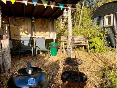 a grill and a brazier in a backyard with a bench at Archie the shepherd’s hut in Penruddock