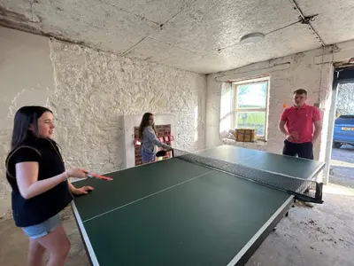 a group of people standing around a ping pong table at Disdow House in Gatehouse of Fleet