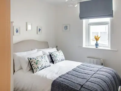 a white bedroom with a bed with pillows and a window at Flag Cottage in Carsethorn