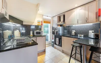 a kitchen with white cabinets and black counter tops at Beagle Cottage in Keswick