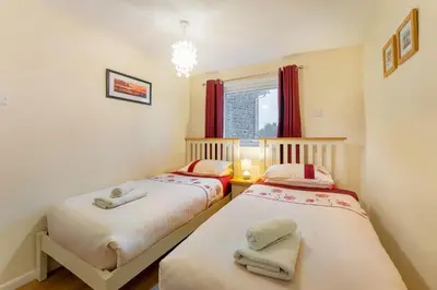 two beds in a small room with red curtains at Sunny Cottage in Keswick