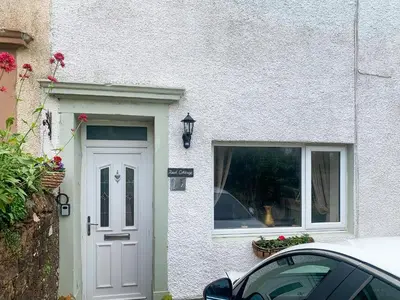 a white house with a door and a window at Reed Cottage in Aspatria