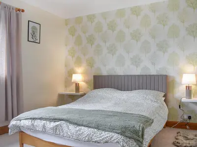 a bedroom with a bed with a green patterned wall at Reed Cottage in Aspatria