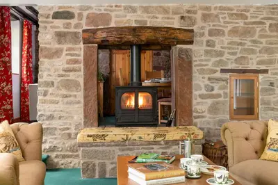 a stone fireplace in a living room with a stove at The Gardeners Cottage, Hutton John is a luxurious cottage with hot tub 10 minutes from Lake Ullswater in Penruddock