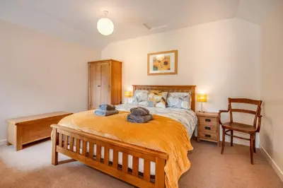 a bedroom with a large bed and a chair at Courtyard Cottages, Garden Cottage in Wigtown