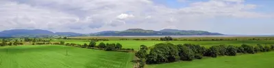 a green field with trees and mountains in the background at Courtyard Cottages, Garden Cottage in Wigtown