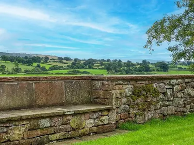 a stone wall with a bench in a field at High House Cottage, Southwaite in a rural setting with garden, BBQ & hot tub in Southwaite