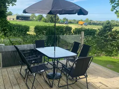a table with chairs and an umbrella on a deck at 23 The Beeches in Gilcrux