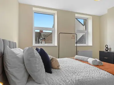 a bedroom with a bed with pillows and two windows at The Penthouse - Crosby St 2 Bed in Maryport