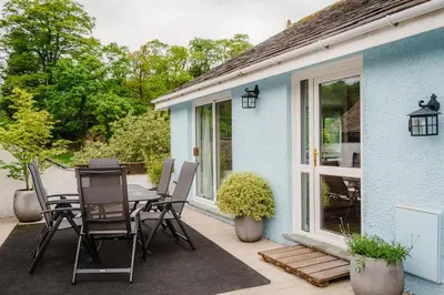 a patio with a table and chairs next to a blue house at Oakbank-Central Grasmere in Grasmere