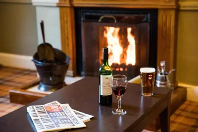a bottle of wine and two glasses on a table with a fireplace at Patterdale Hotel in Patterdale