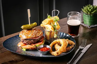 a plate with a hamburger and onion rings and a glass of beer at The Inn On The Lake in Glenridding
