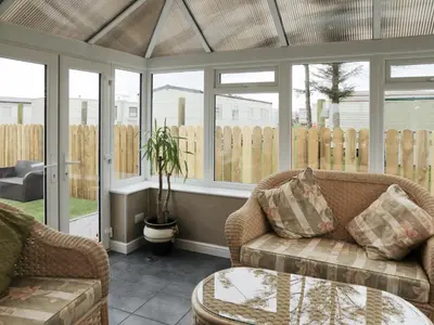 a conservatory with a couch and a table and windows at Firth Lodge in Mainsriddle