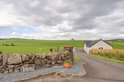 a stone wall next to a road in a field at Berryrigg Cottage in Dumfries