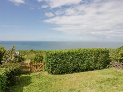 a hedge in a yard with the ocean in the background at Victroneen Cottage in Whitehaven