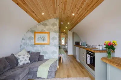 a living room with a couch and a kitchen at The Galloway Steading -The Hedgehog's Hideout family cabin with Hot Tub and Fire Pit in Glenluce