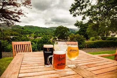 two glasses of beer sitting on a wooden table at The Swan at Grasmere- The Inn Collection Group in Grasmere