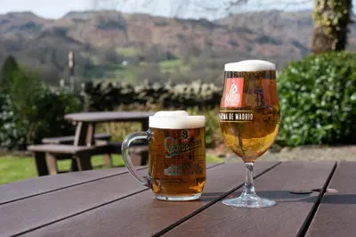 two glasses of beer sitting on a wooden table at The Swan at Grasmere- The Inn Collection Group in Grasmere