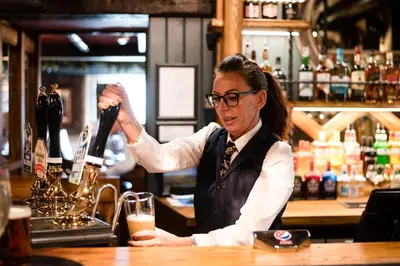 a woman is pouring a drink in a bar at The Swan at Grasmere- The Inn Collection Group in Grasmere