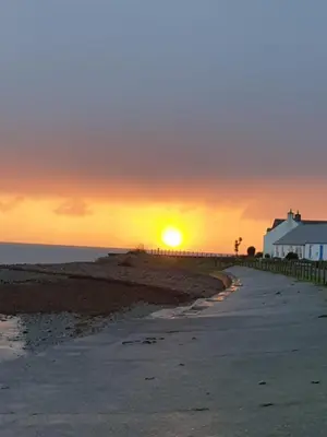 a sunset over a beach with a house and the ocean at The Old Cornstore a beautiful Suite overlooking the sea in Drummore