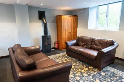 a living room with two leather chairs and a stove at Weirside, Chapel Stile in Ambleside