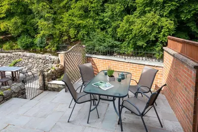 a patio with a table and chairs and a brick wall at Lydia's River Cottage in Keswick