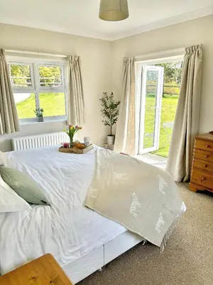 a white bed in a bedroom with windows at Kionslieu Farm Cottages in Foxdale