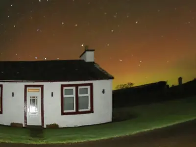 a small white house in a field at night at Kilquhanity Cottage in Castle Douglas