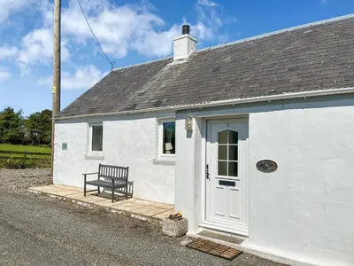 a black bench sitting outside of a white building at Rose Cottage in Port Logan