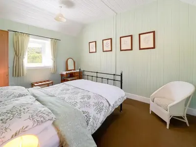 a bedroom with a bed and a chair and a window at Rose Cottage in Port Logan