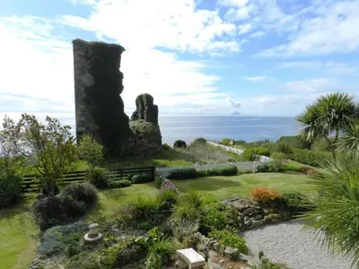 a garden with a stone tower and the ocean at Castleside Croft in Kildonan