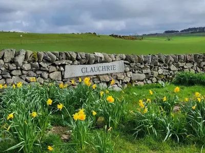a stone wall with a sign in a field of flowers at Large country house with garden, outdoor spa area & games room with Hot Tub and Fire Pit in Wigtown