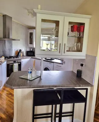 a kitchen with white cabinets and a island with two bar stools at Top Lodge in Newton Stewart