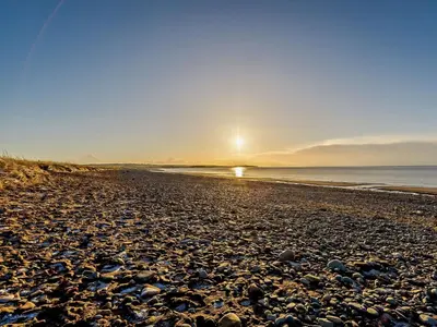 a pebble beach with the sun setting over the ocean at 1 Bed in Allonby 95499 in Allonby