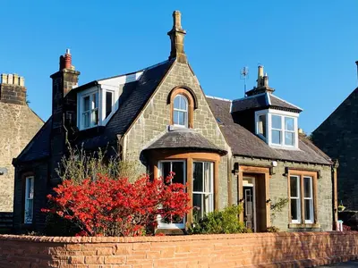 a house with a red bush in front of it at Burnbank Bed and Breakfast in Moffat