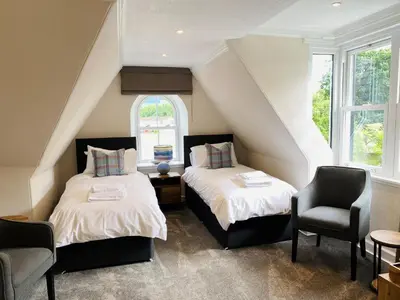 a attic bedroom with two beds and a chair at Burnbank Bed and Breakfast in Moffat
