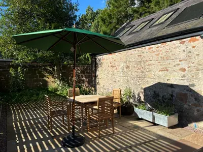 a table and chairs under an umbrella on a patio at Stable Cottage in Lockerbie