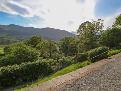 a stone path with trees and mountains in the background at Bluebells in Ambleside